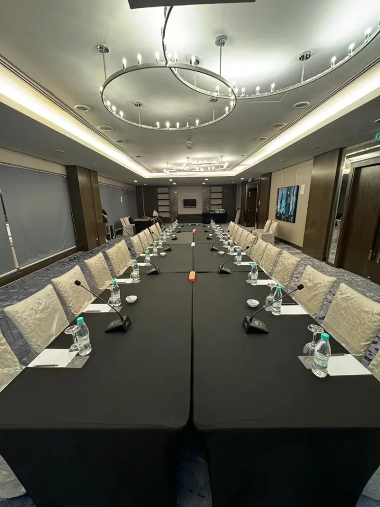 The image shows the meeting location, with gooseneck mics at every participant's desk and sound system